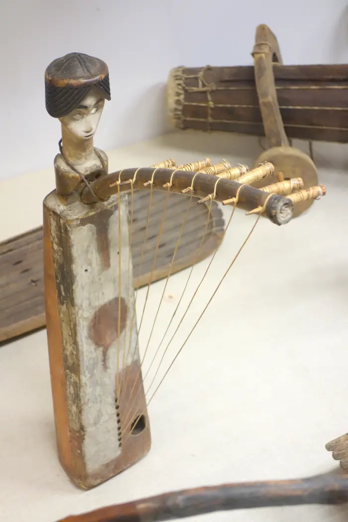 A Fang harp standing upright in a museum vitrine: a tall carved neck above a skin-covered body, strings running its length, lit against a dark background.