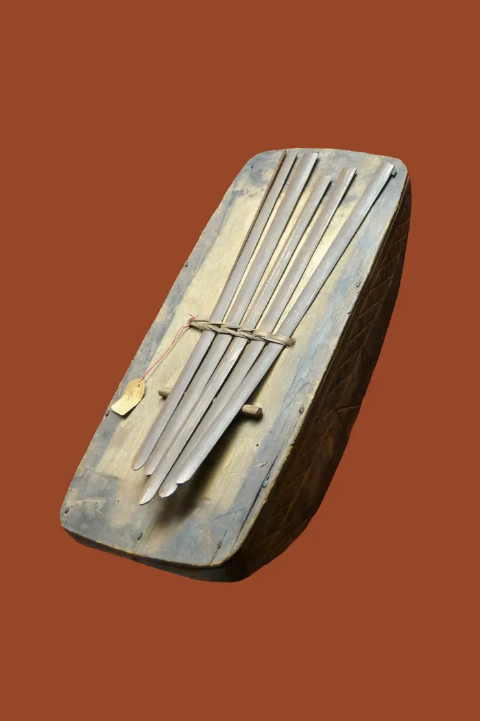 A small lamellophone: a carved wooden body with a row of thin metal tongues of graduated length fixed across a bridge, played with the thumbs.